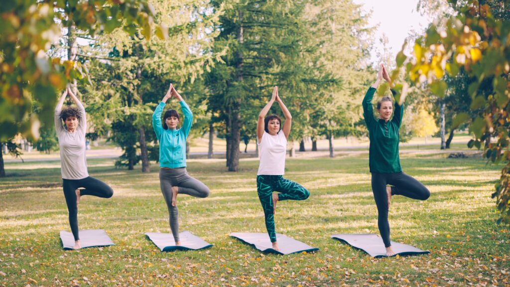 Benefits of doing yoga in daily life Four women performing yoga in a tranquil park during a sunny fall day.