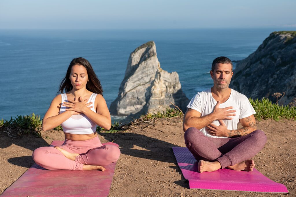 Breathing Techniques in Yoga: The Foundation of Physical and Mental Well-Being Man and woman practicing meditation on yoga mats by the ocean in Portugal.